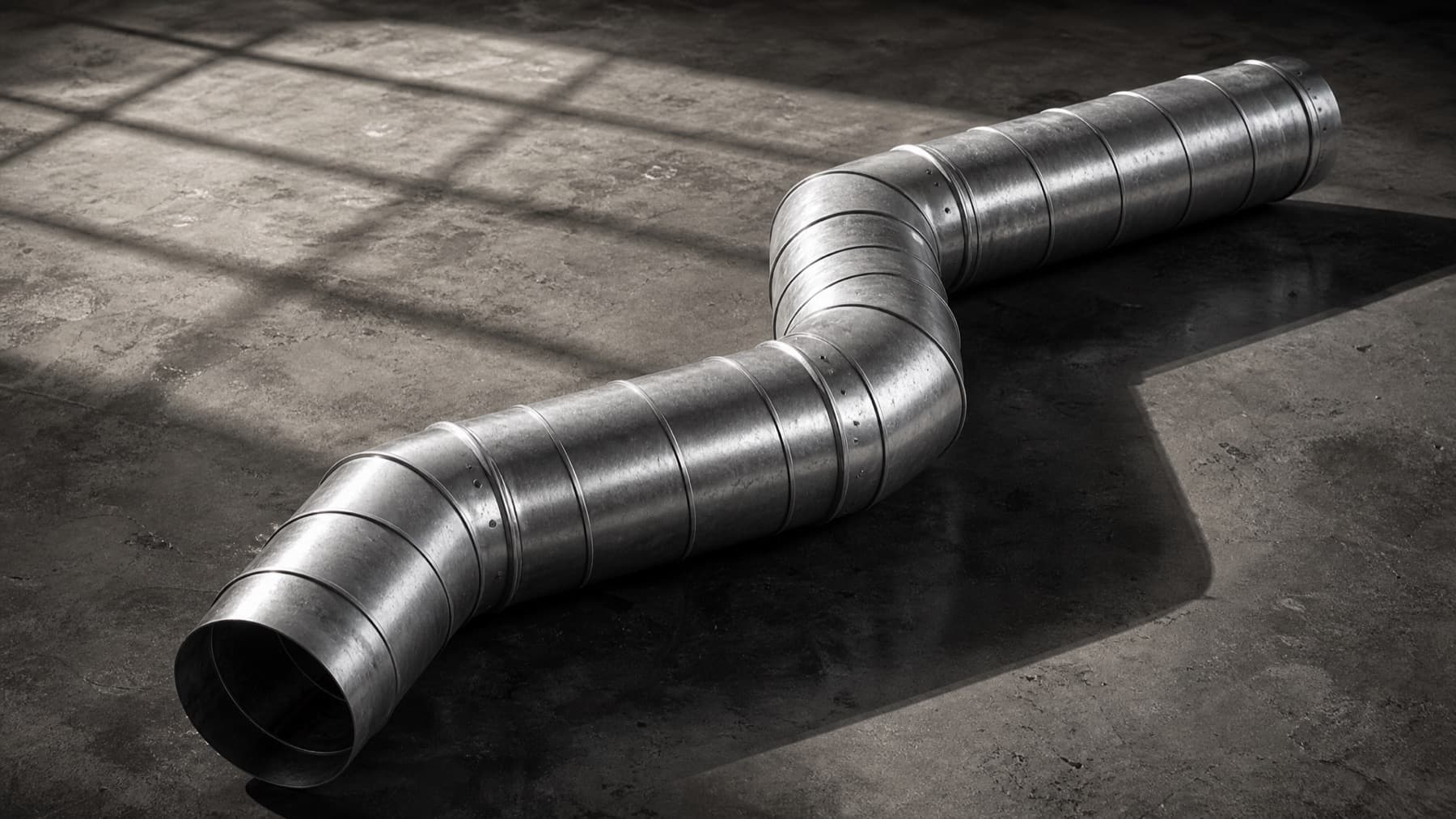 A two-elbow offset run in round spiral duct, assembled on a concrete shop floor in raking window light.